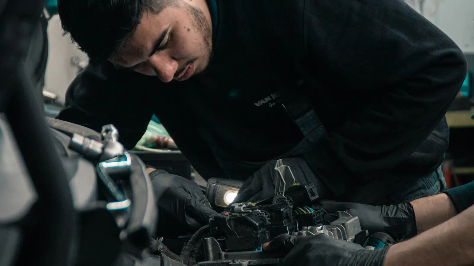Mechanic wearing gloves repairs car engine inside a garage with focused attention on parts and tools.