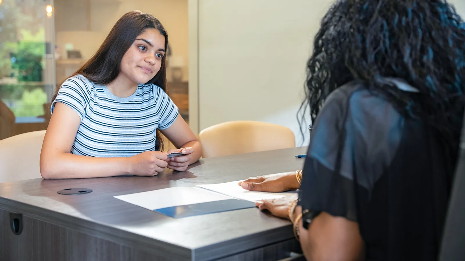 Young woman in striped shirt attentively listening during a meeting across a table with another person.