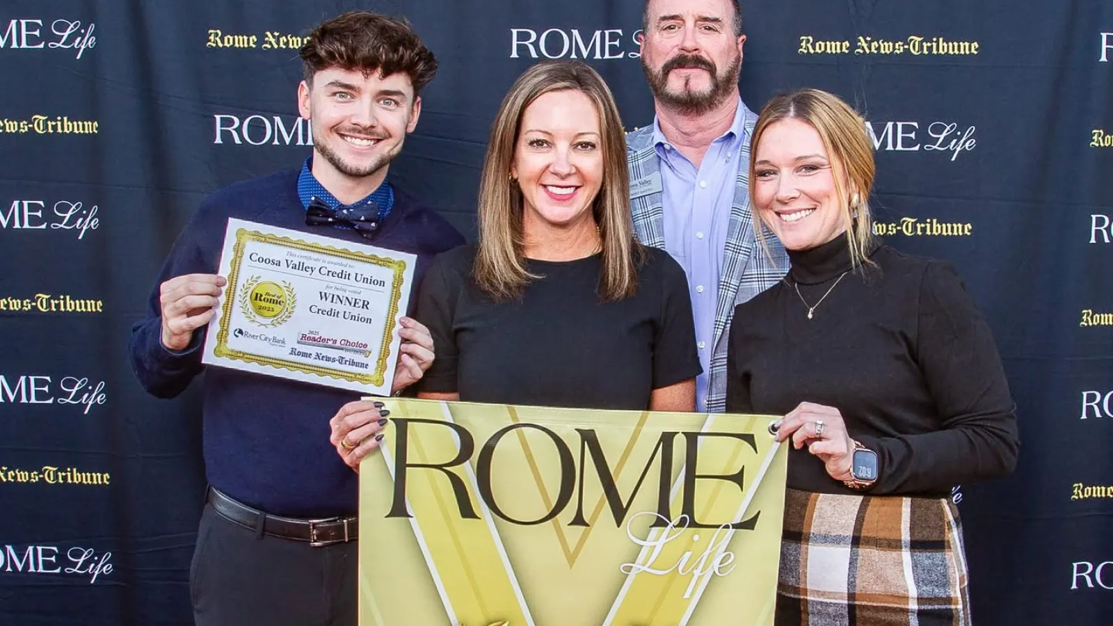 Joshua, Emily, Robert, and Paige holding Best of Rome 2025 winner banners on red carpet at Rome Life event for Coosa Valley Credit Union