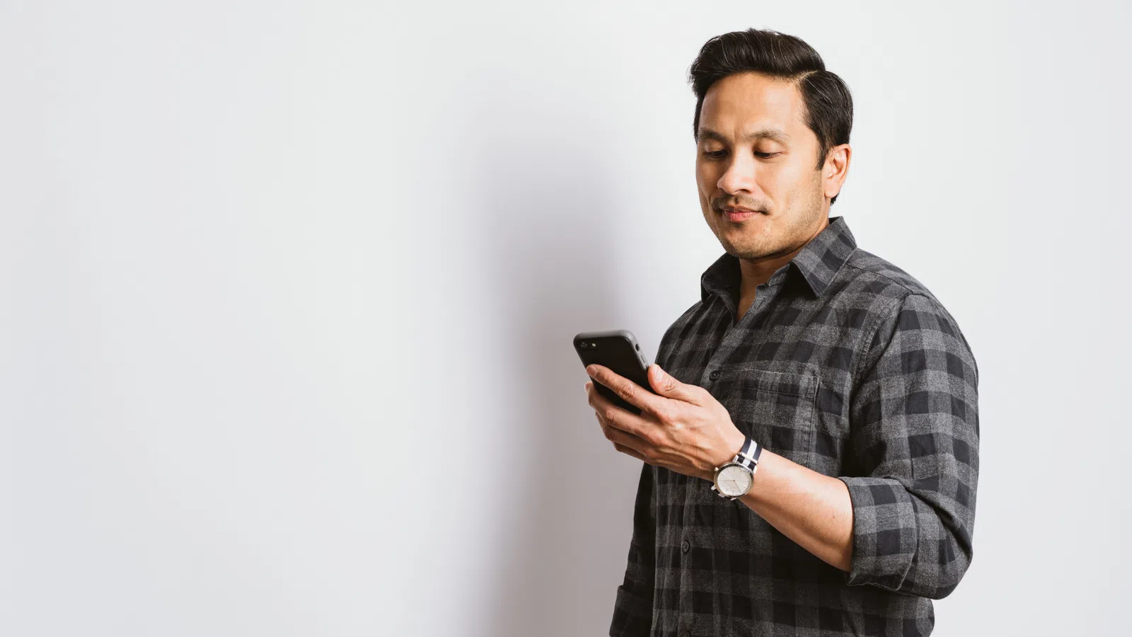 A man in a plaid shirt checks his phone against a plain white background, exuding a relaxed vibe.