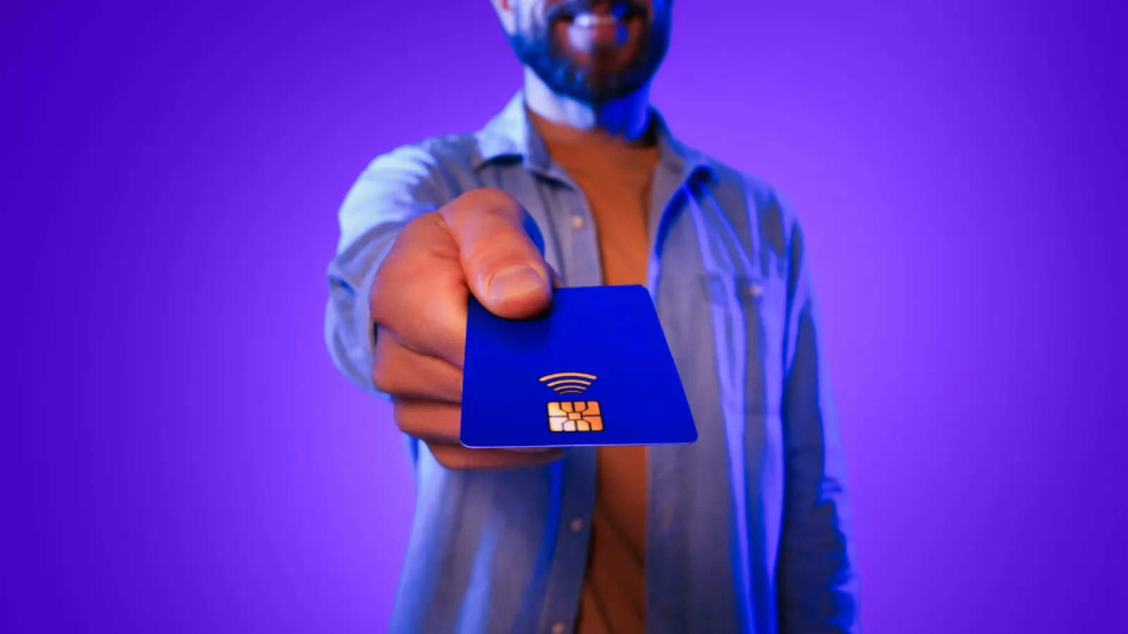 Man holding a blue contactless credit card towards the camera against a purple background