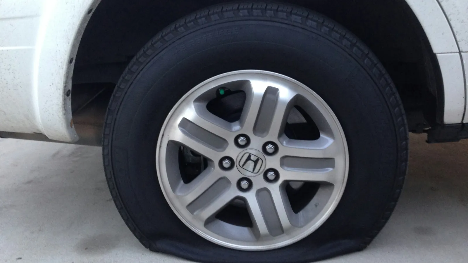 Flat tire on a white Honda vehicle with a silver alloy wheel parked on concrete ground.
