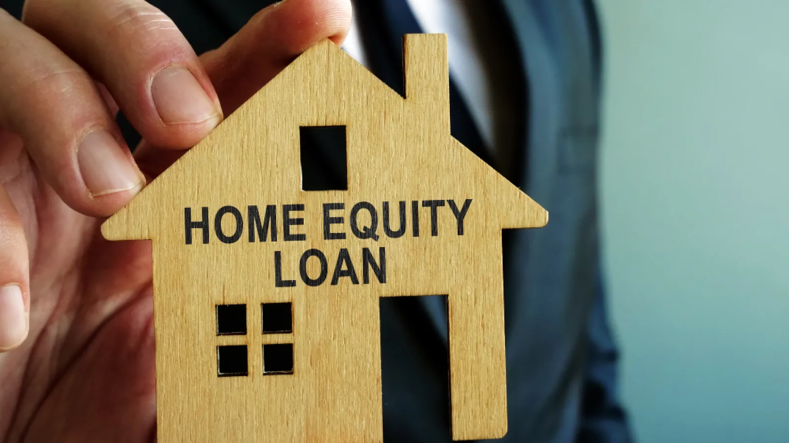 Businessman holding wooden house model with Home Equity Loan text against blurred background