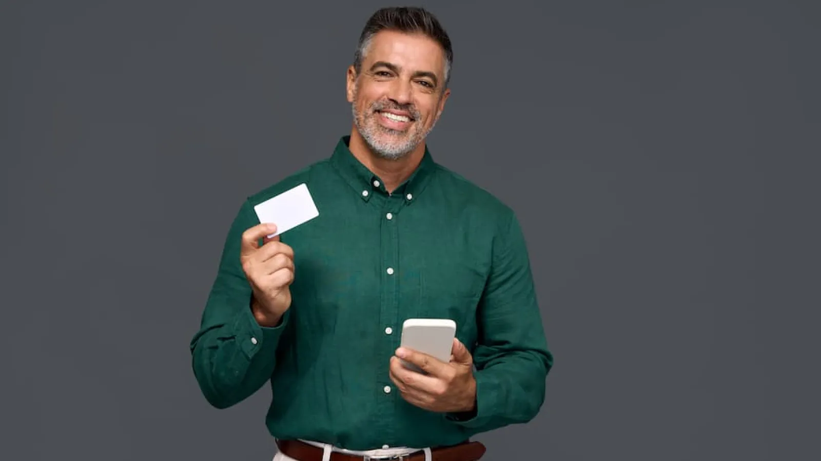 Smiling man holding a smartphone and a blank white credit card, illustrating the advantages of credit unions over banks for personal finance.