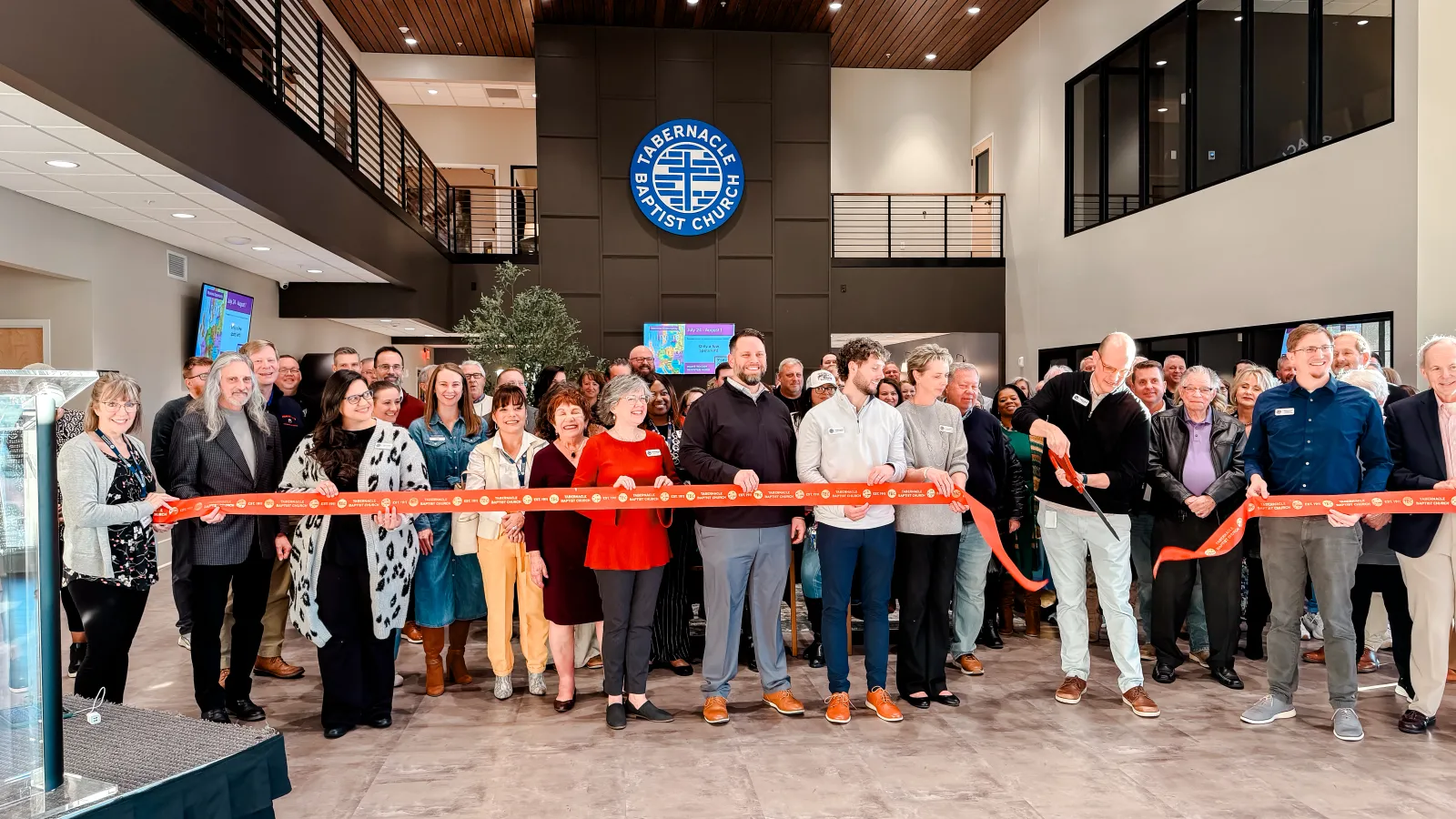 Group of people gathered for a ribbon-cutting ceremony inside a modern church lobby with Tabernacle Baptist Church signage.