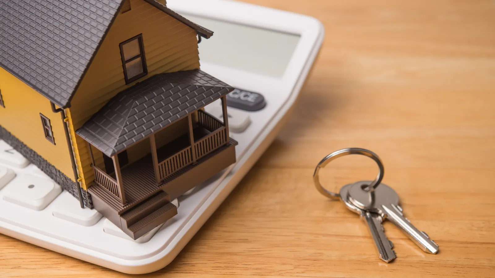 Miniature house on a calculator with keys on a wooden table symbolizing home finance or mortgage.