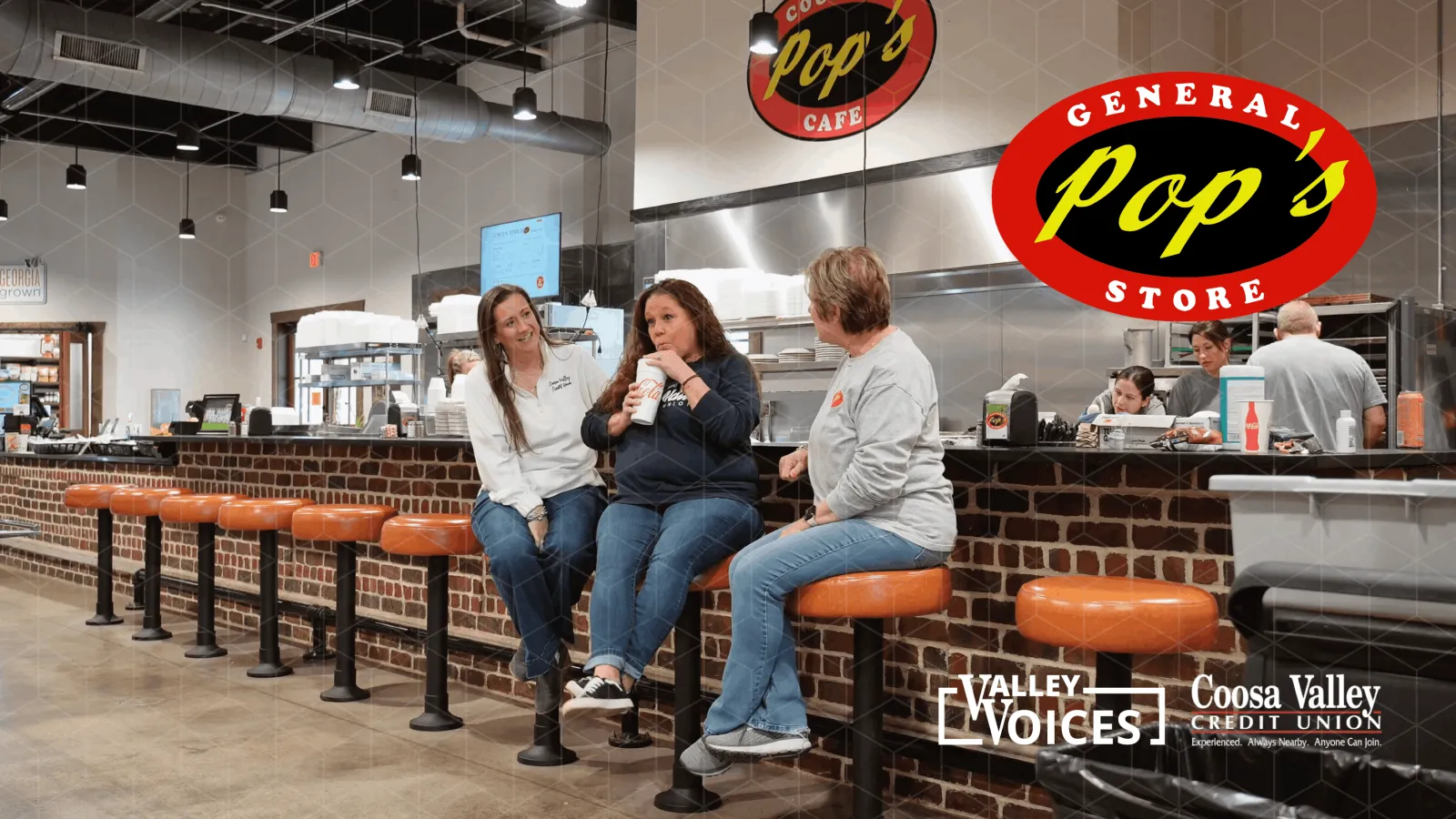 Three women sitting on orange stools at Pop's General Store counter, drinking and chatting in a bright cafe