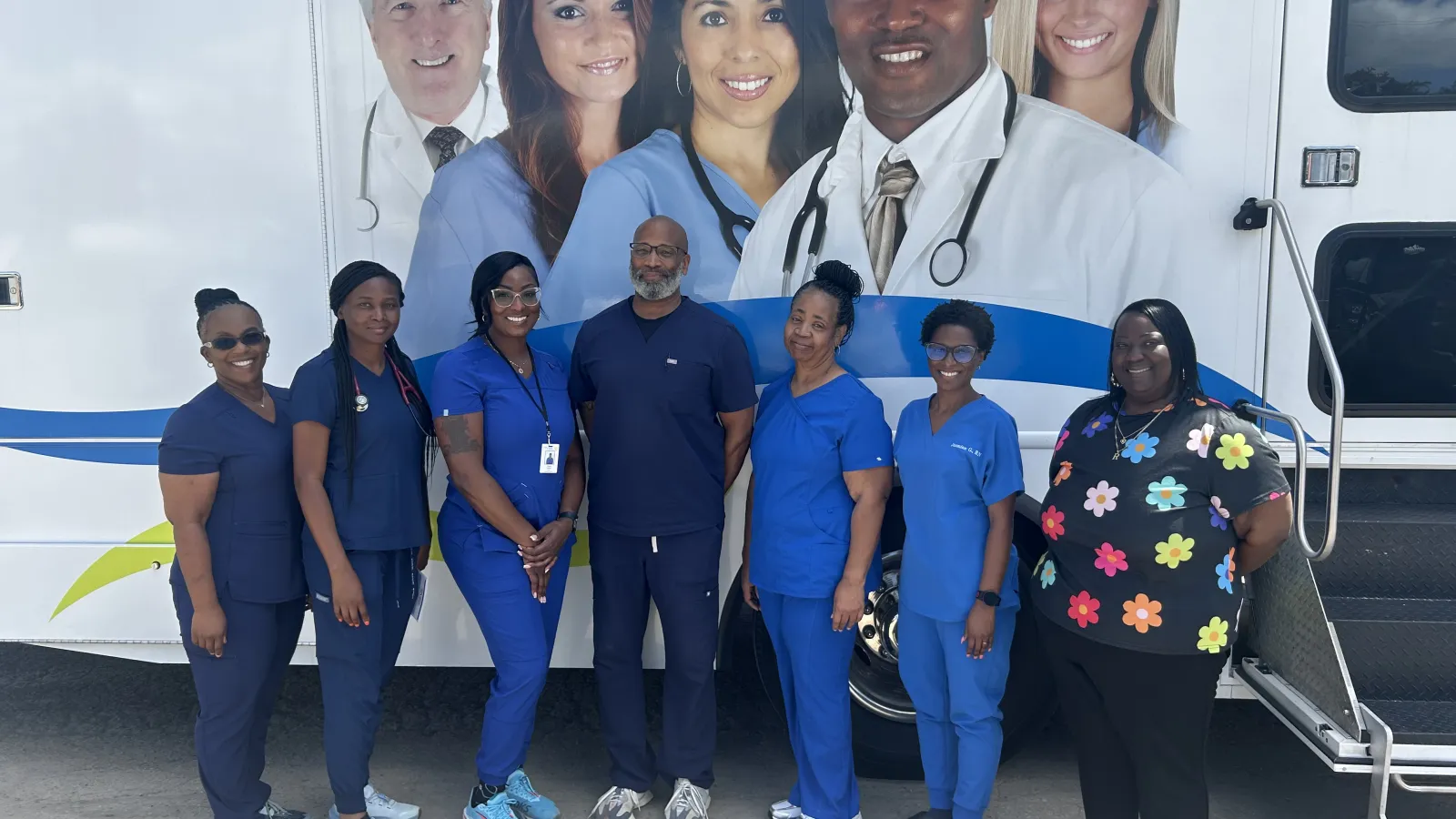 Medical team in scrubs standing outside a mobile clinic van with healthcare professionals' images on it.