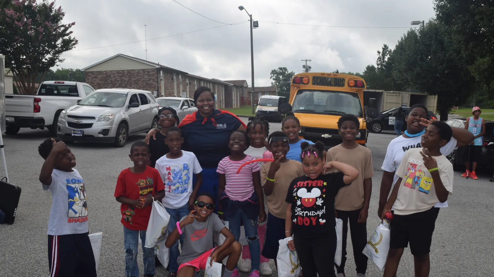 Group of happy children and an adult posing outdoors near a school bus on a cloudy day