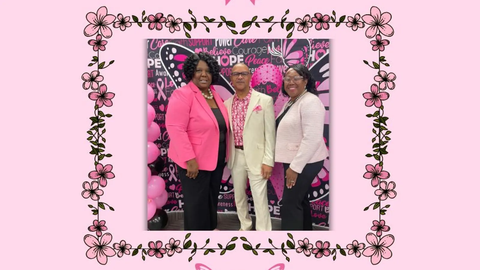 Three people pose in pink-themed attire for breast cancer awareness with butterfly and ribbon decorations.