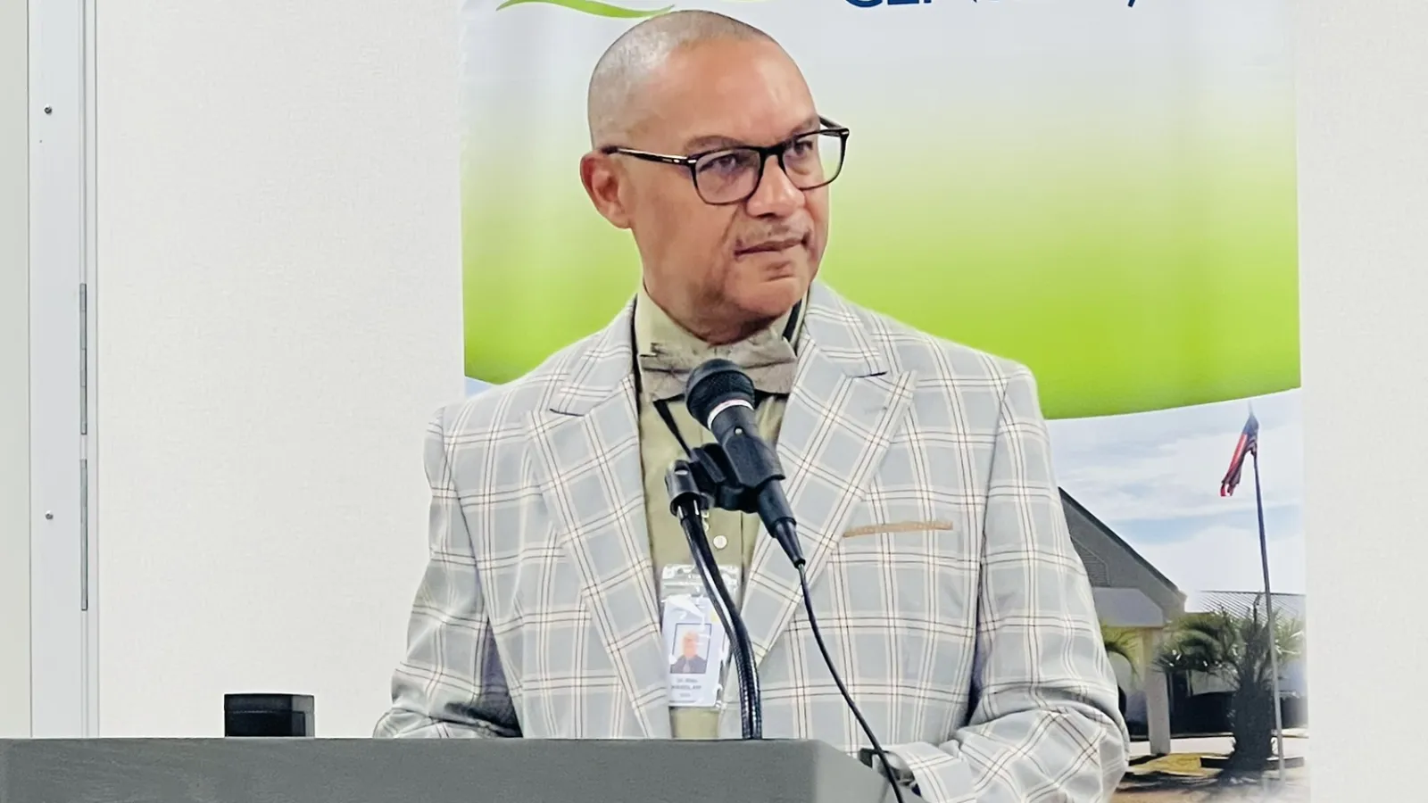 Man in glasses and plaid suit speaking at a podium with Family Health Centers banner in background.