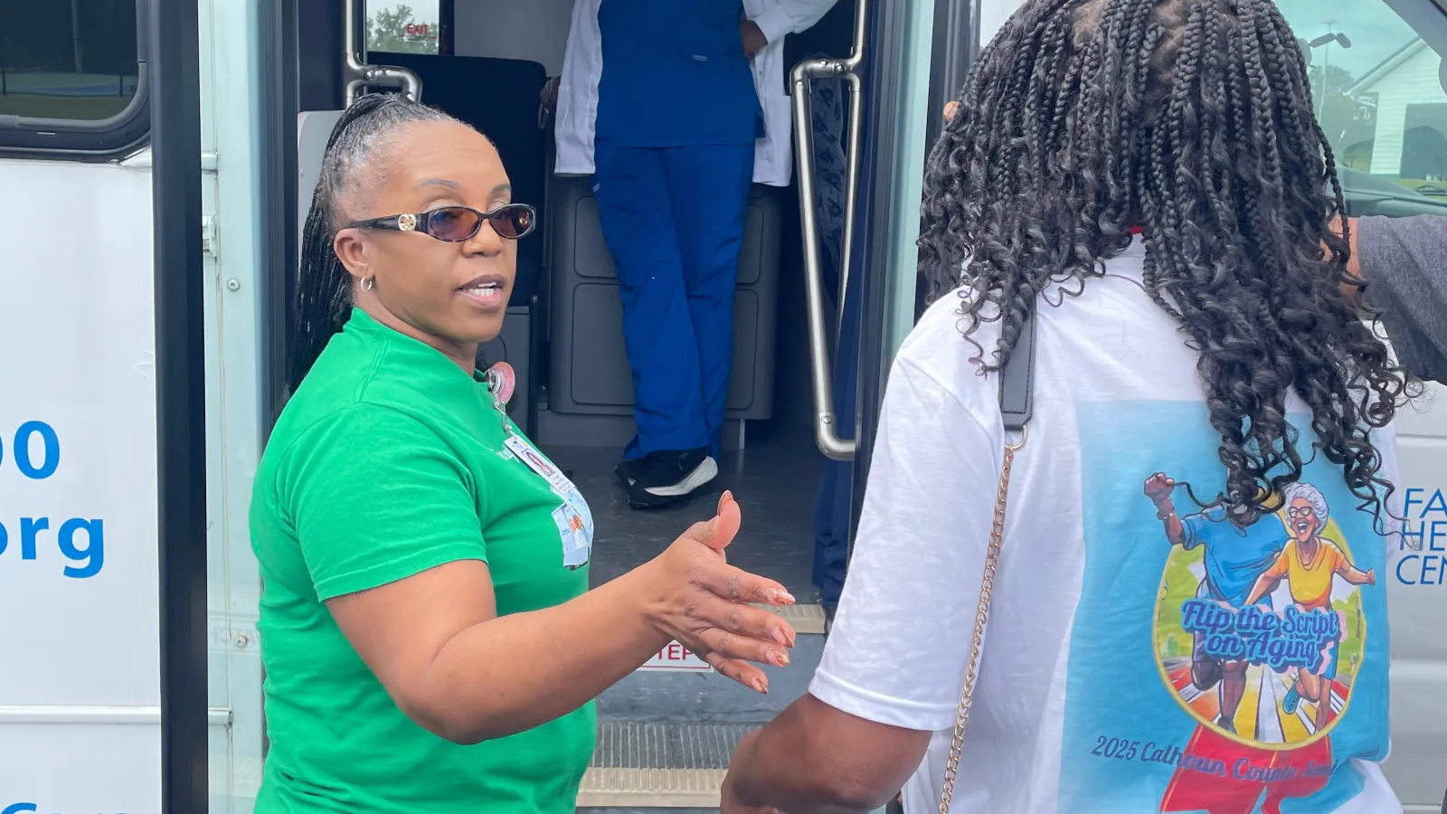 Two women talking outside a mobile medical van with a healthcare worker standing inside the vehicle