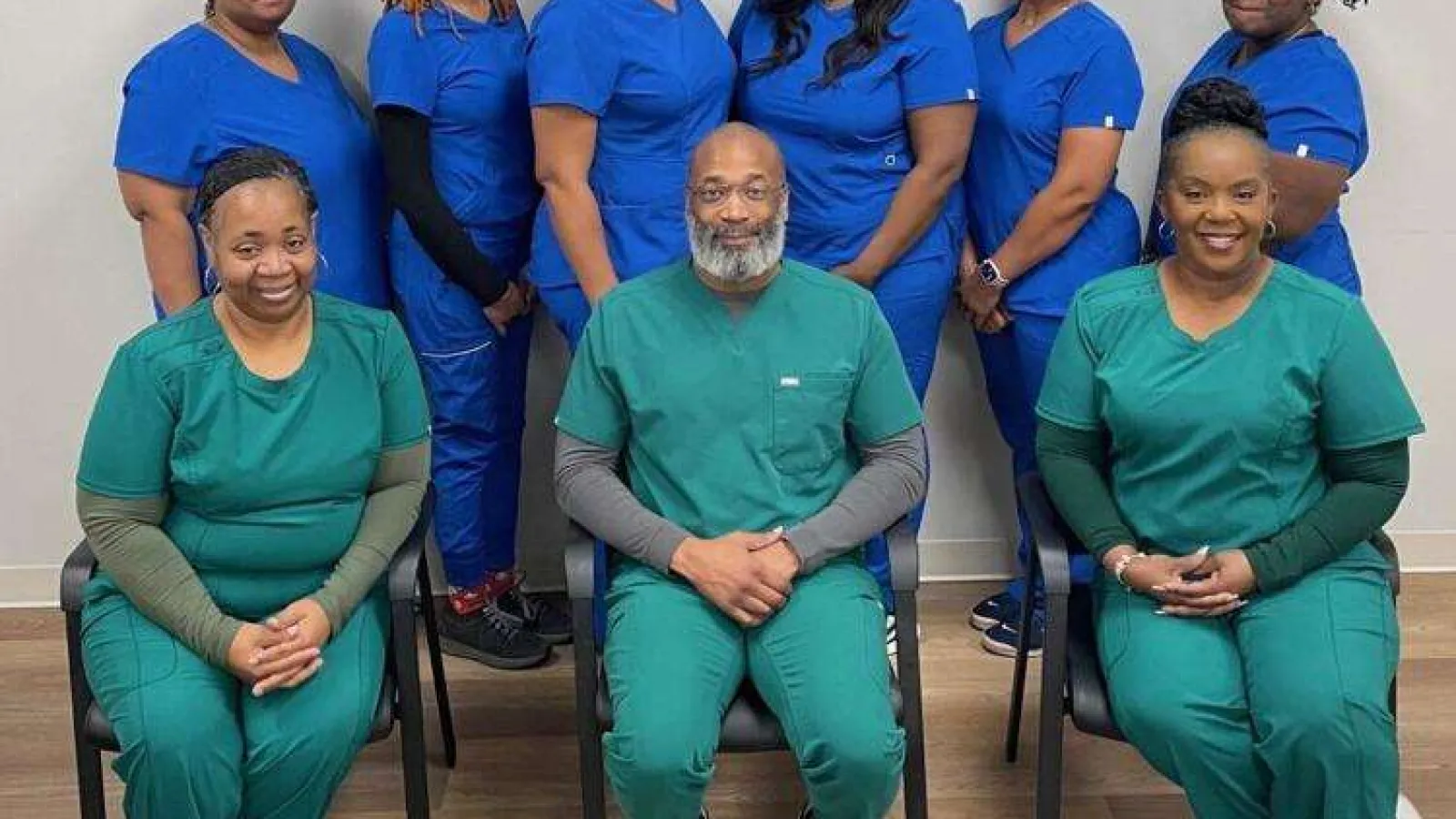 Group photo of healthcare professionals in blue and green scrubs smiling in a clinical setting