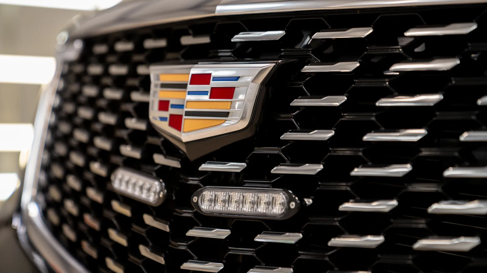 Close-up of Cadillac emblem on black grille with chrome accents and lights of a luxury vehicle