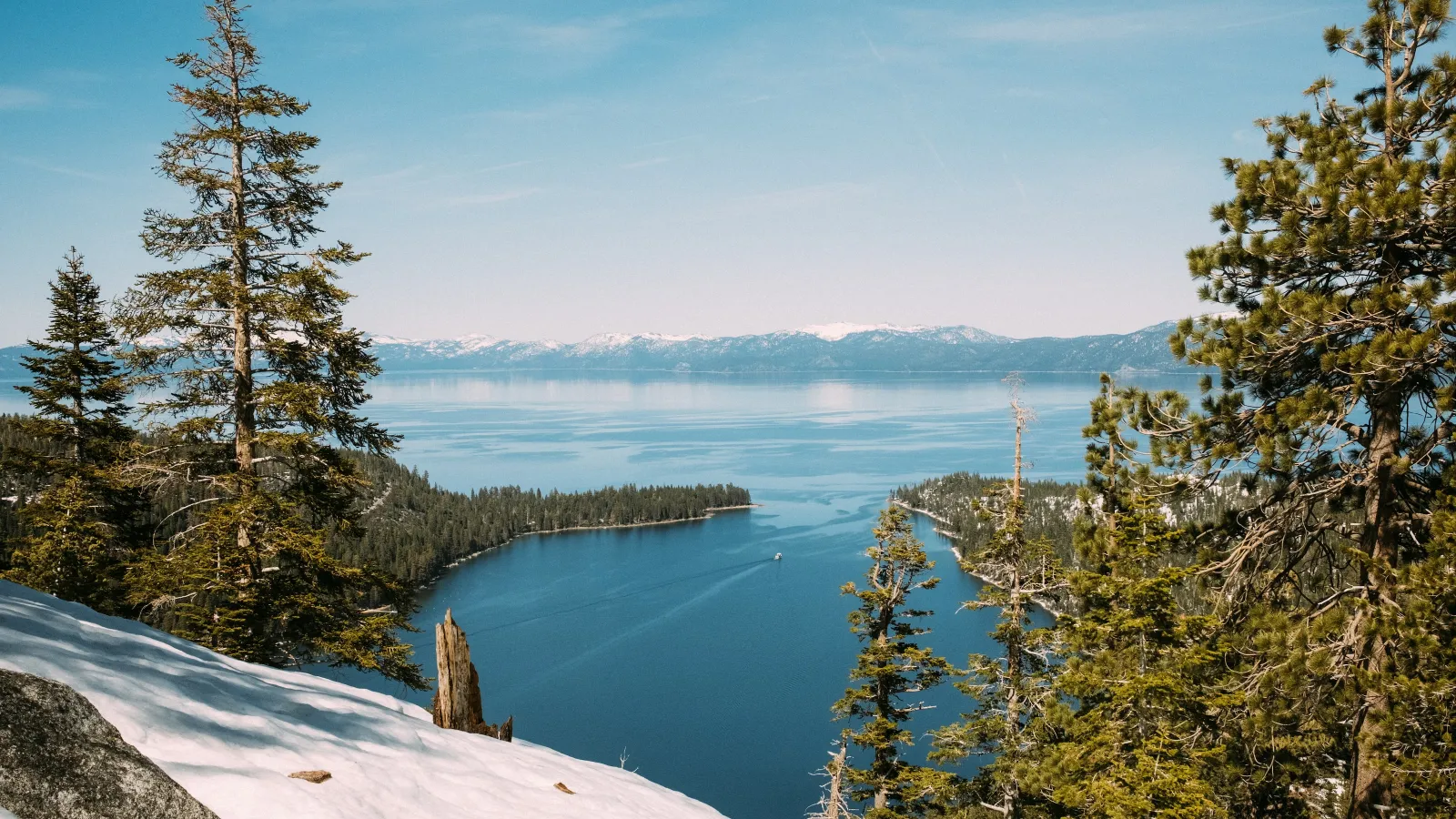 a snowy landscape with trees and a body of water in the background in California