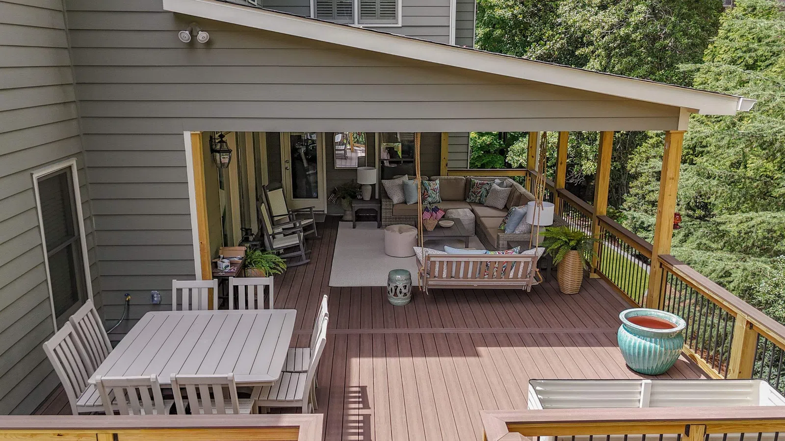 Spacious outdoor deck with wooden flooring, dining table, seating area, and lush green trees surrounding the space