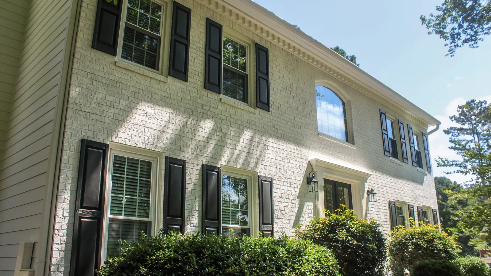 Close-up of green shingle siding on a house with a window and bare tree branches in the background.