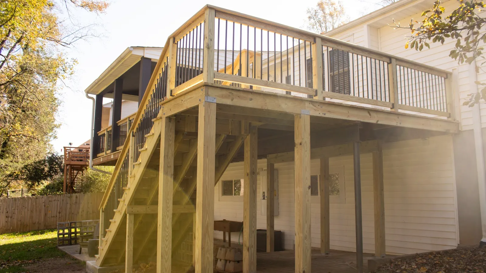 Newly built wooden deck with stairs and metal railing attached to a white house in sunny backyard.