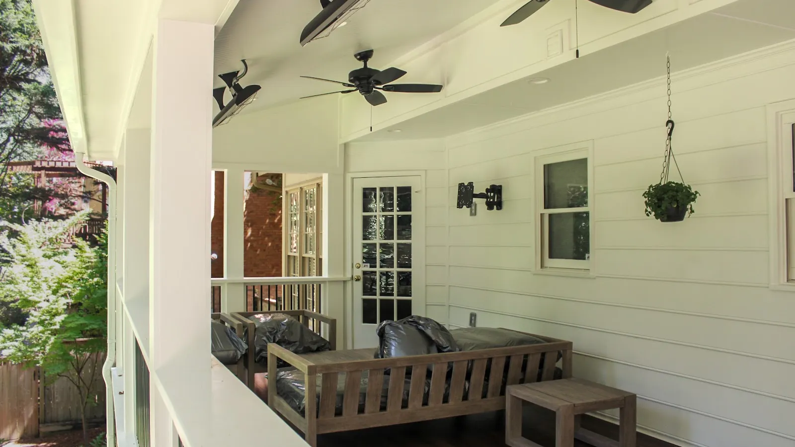 White house dormer windows with black roof shingles surrounded by green trees under blue sky.