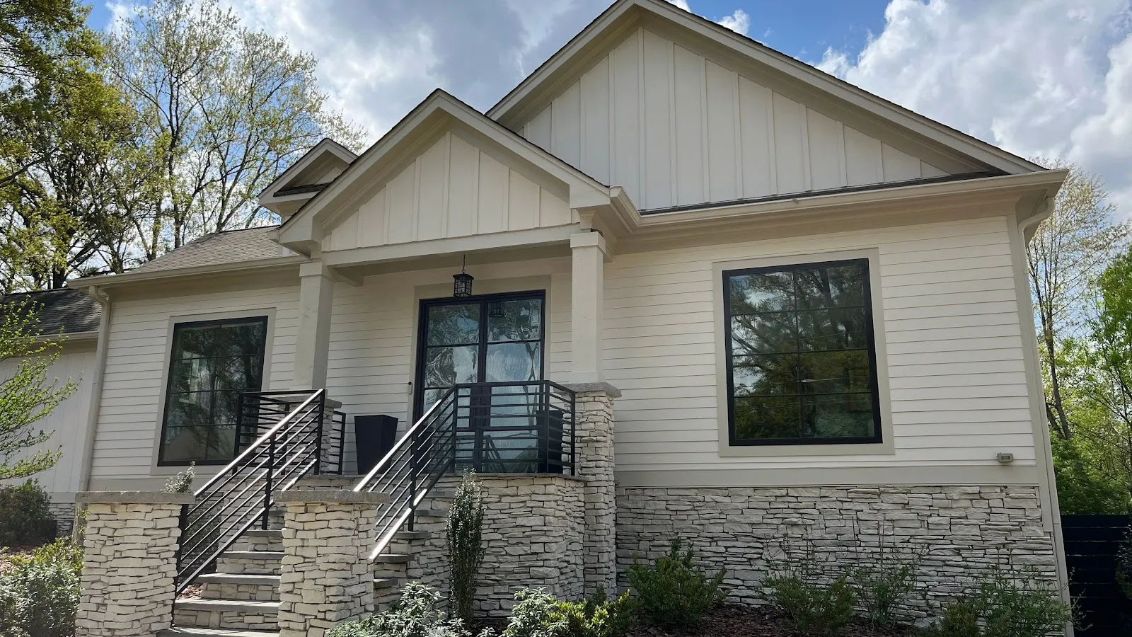 White house dormer windows with black roof shingles surrounded by green trees under blue sky.