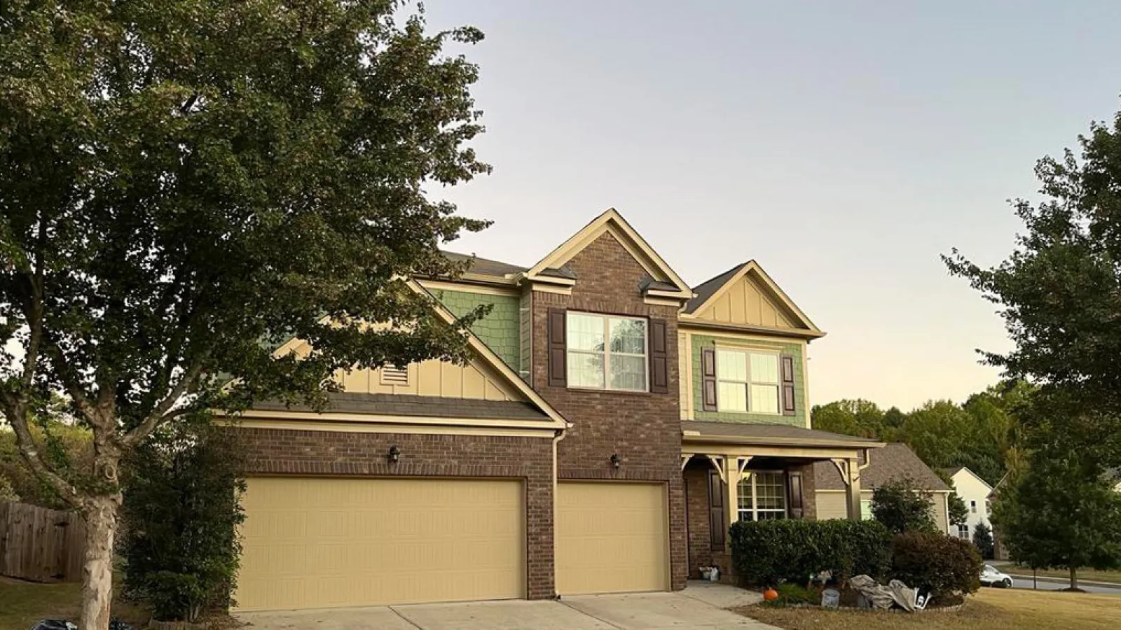 Close-up of green shingle siding on a house with a window and bare tree branches in the background.