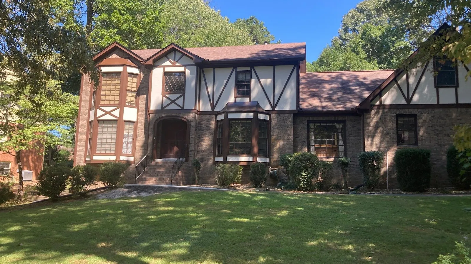 Close-up of green shingle siding on a house with a window and bare tree branches in the background.