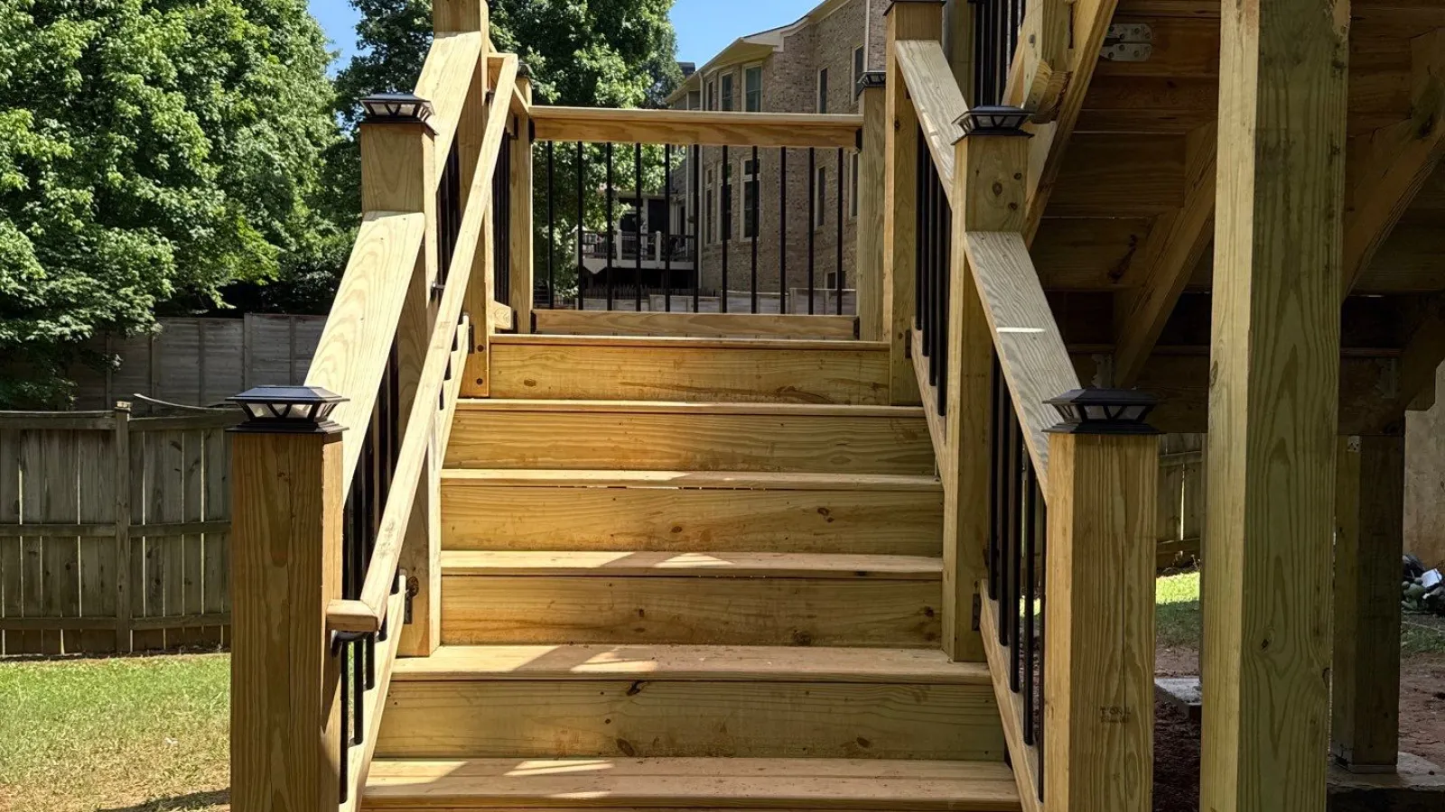 White house dormer windows with black roof shingles surrounded by green trees under blue sky.