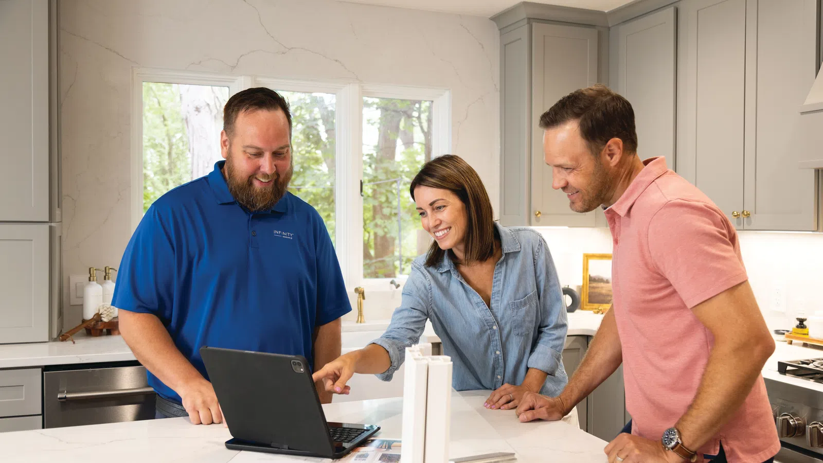 Couple consulting a professional on a laptop in a modern kitchen with white marble countertops.