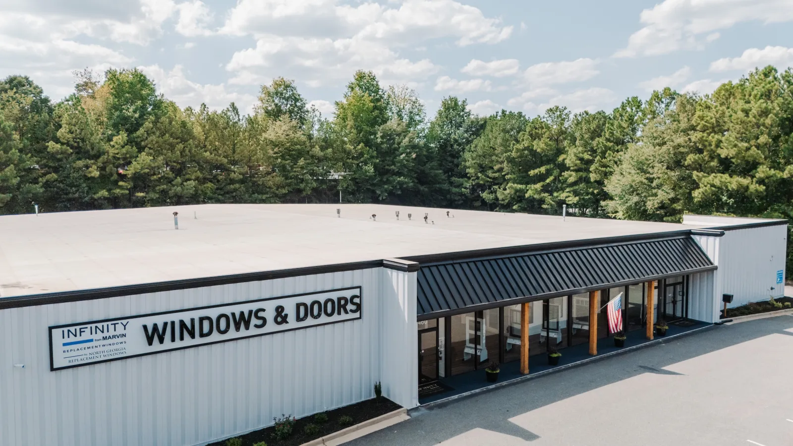 Exterior view of Infinity Windows & Doors showroom with a black awning and surrounding trees under a partly cloudy sky