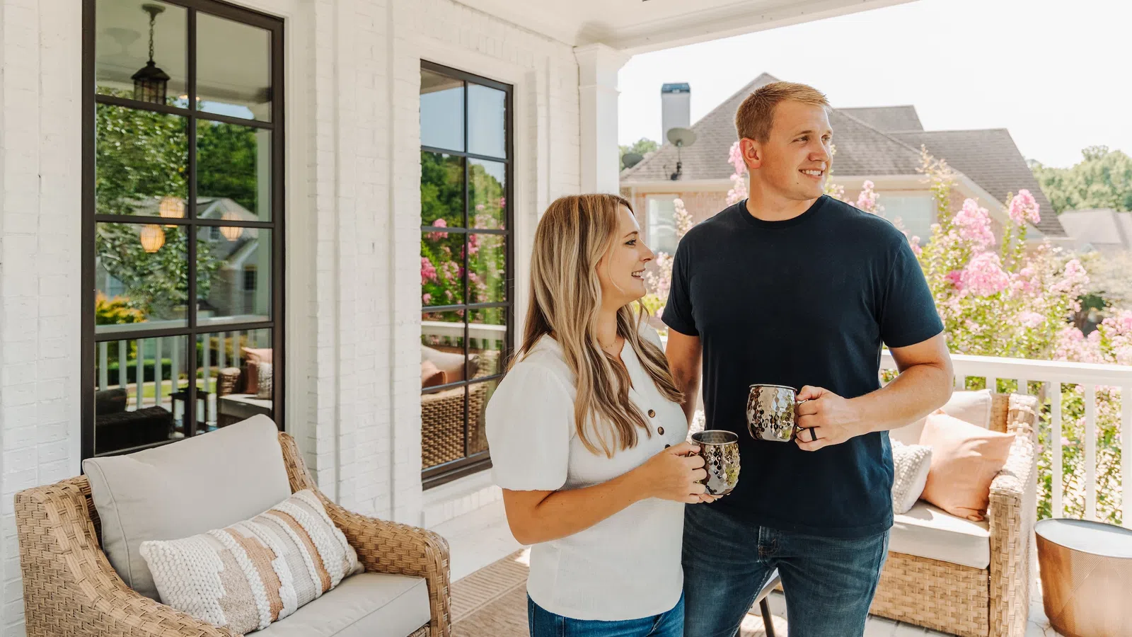 Couple enjoying morning coffee on a cozy porch with wicker furniture and blooming flowers in the background
