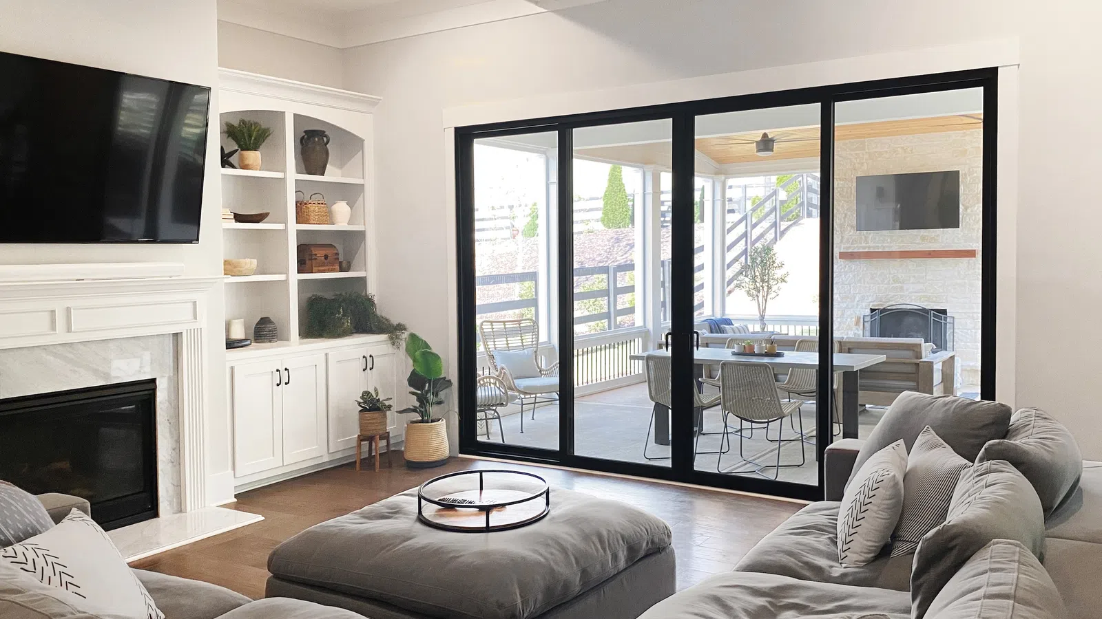 Modern living room with gray sectional sofa, ottoman, built-in shelves, fireplace, and sliding glass doors to patio.