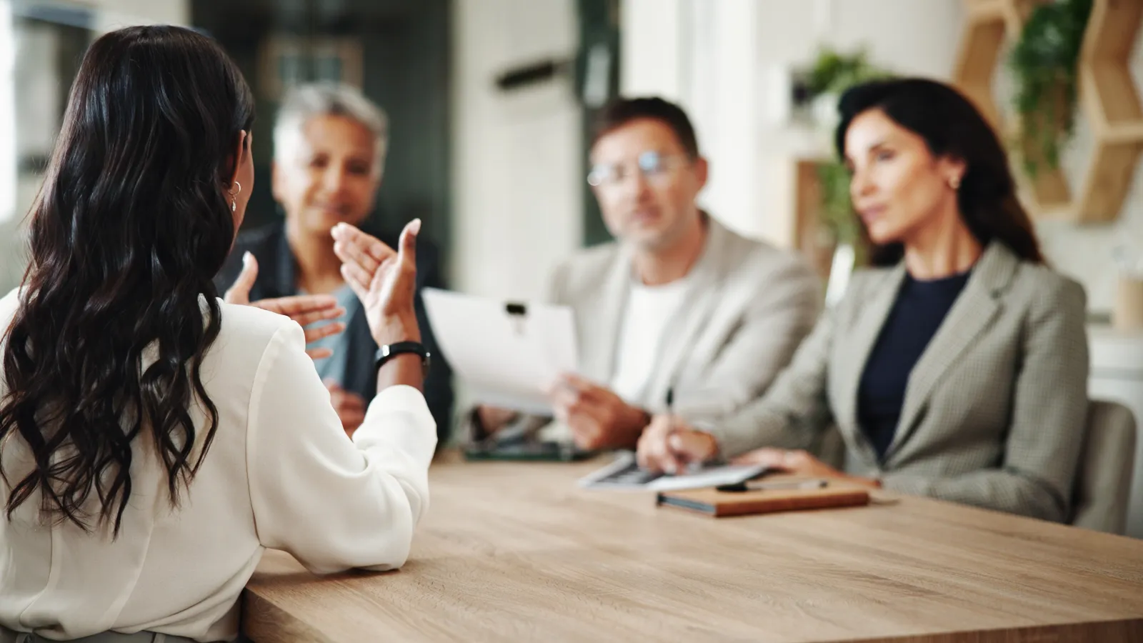 Woman in white blouse explaining to three colleagues during a business meeting around a wooden table.