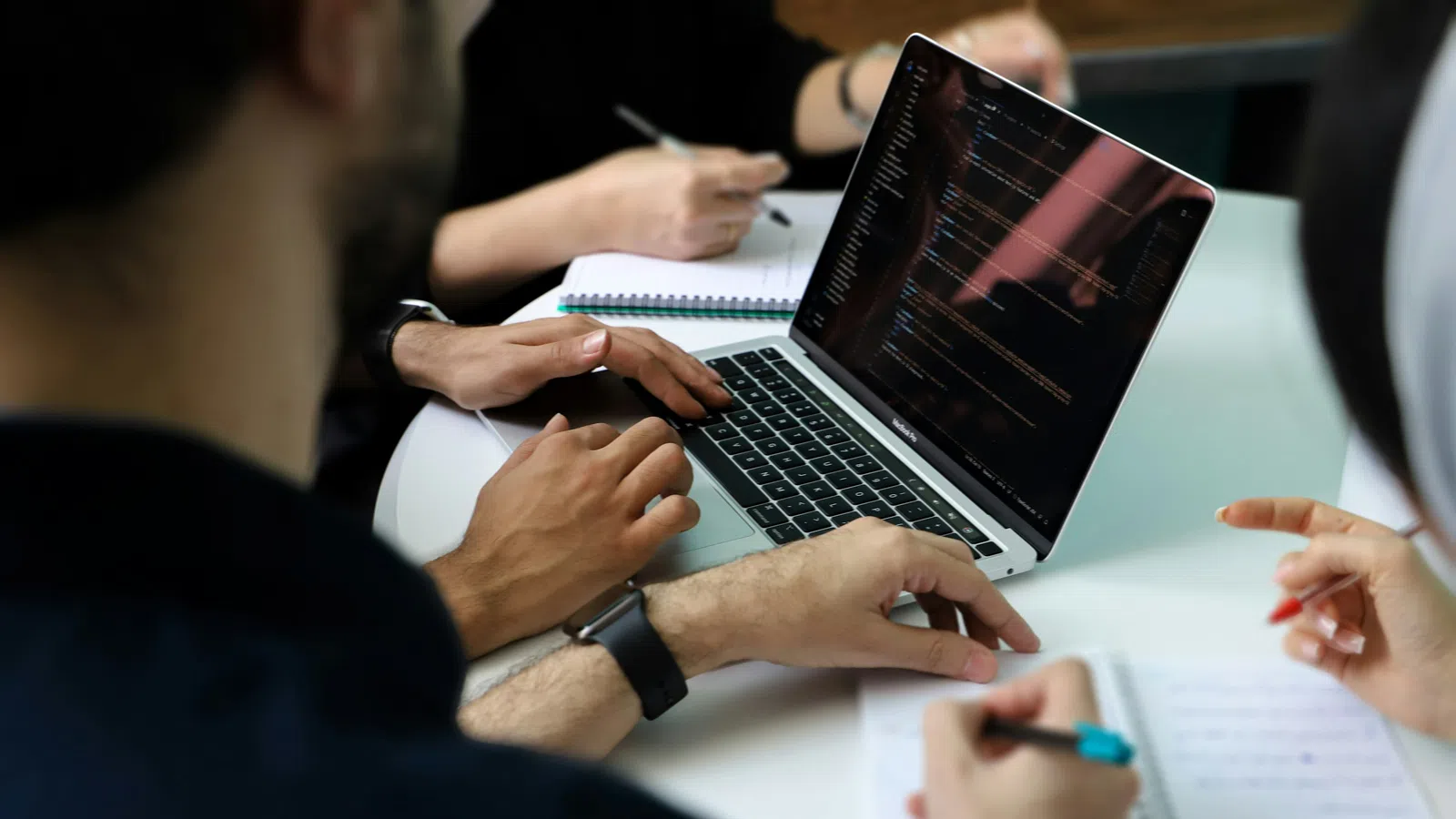 Team collaborating with laptop showing code while taking notes in a meeting setting