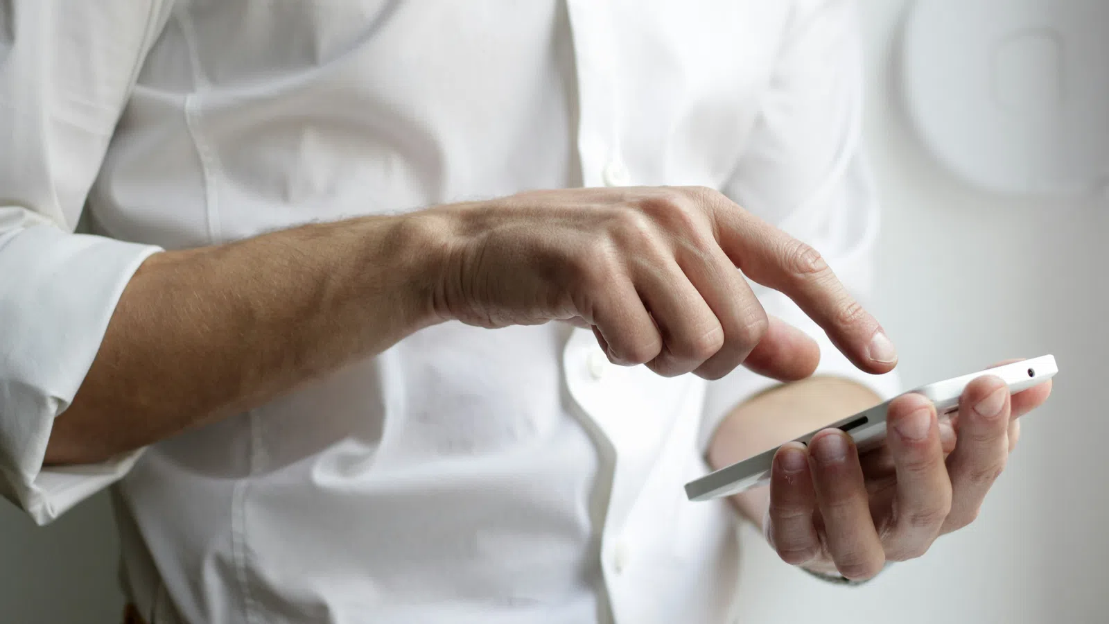 Person in white shirt using a smartphone with one hand tapping the screen indoors.