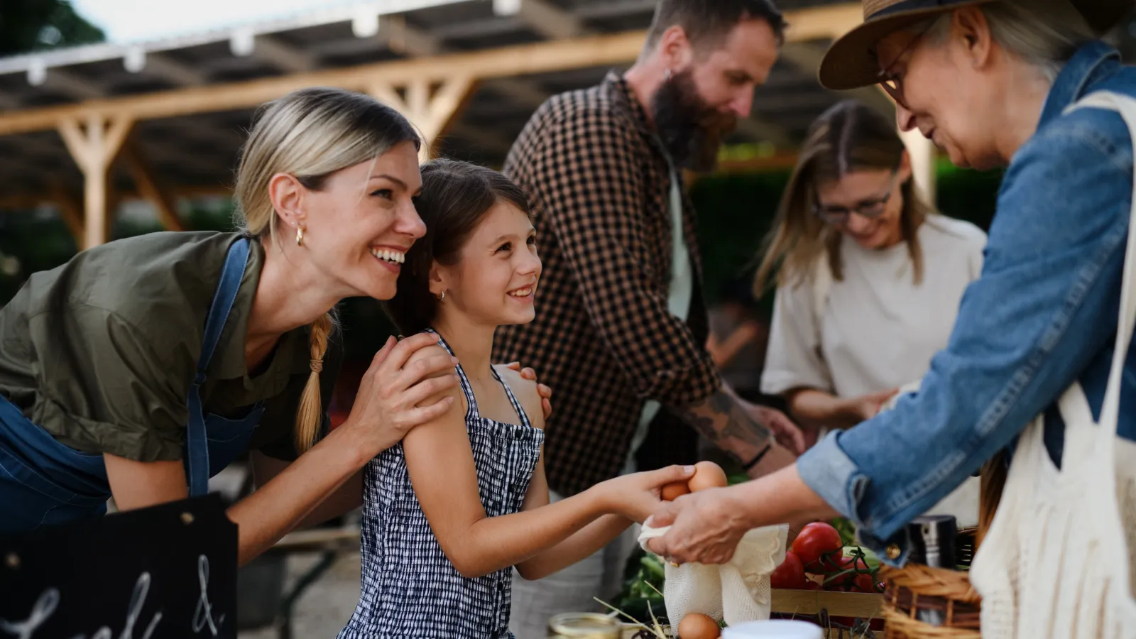 Happy mother and daughter buying fresh eggs from a vendor at a local outdoor farmers market.
