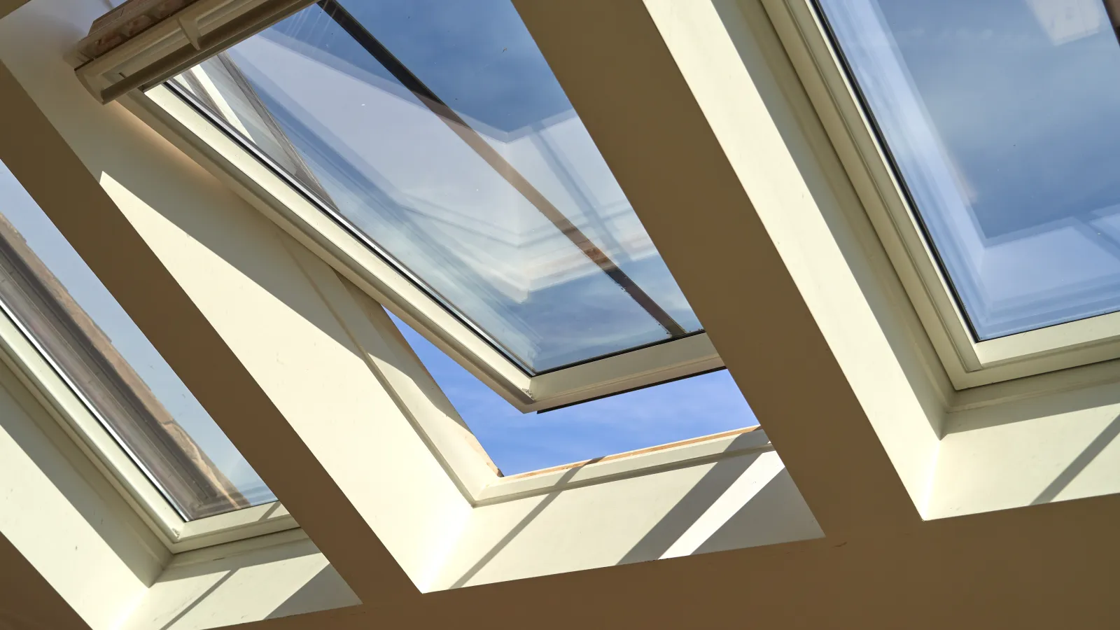 Three skylight windows installed in a ceiling with one window open showing blue sky outside.