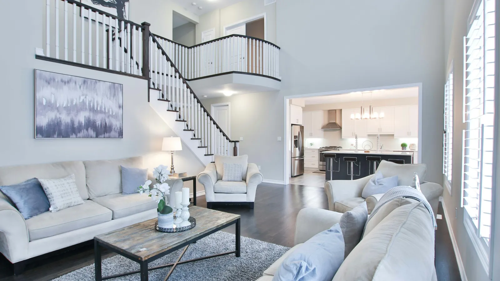 Bright modern living room with gray sofas, wooden coffee table, staircase, and open kitchen in the background