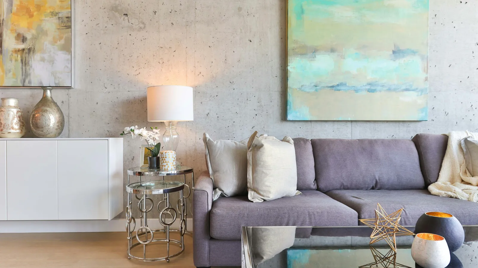 Modern living room with gray sofa, abstract art, metallic side tables, decorative vases, and soft lighting.