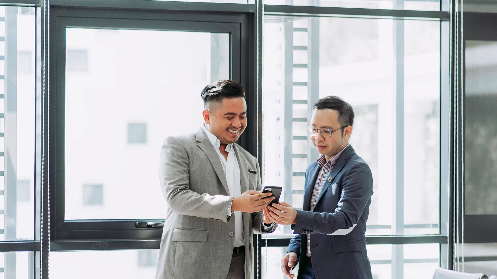 a couple of men in suits looking at a cell phone