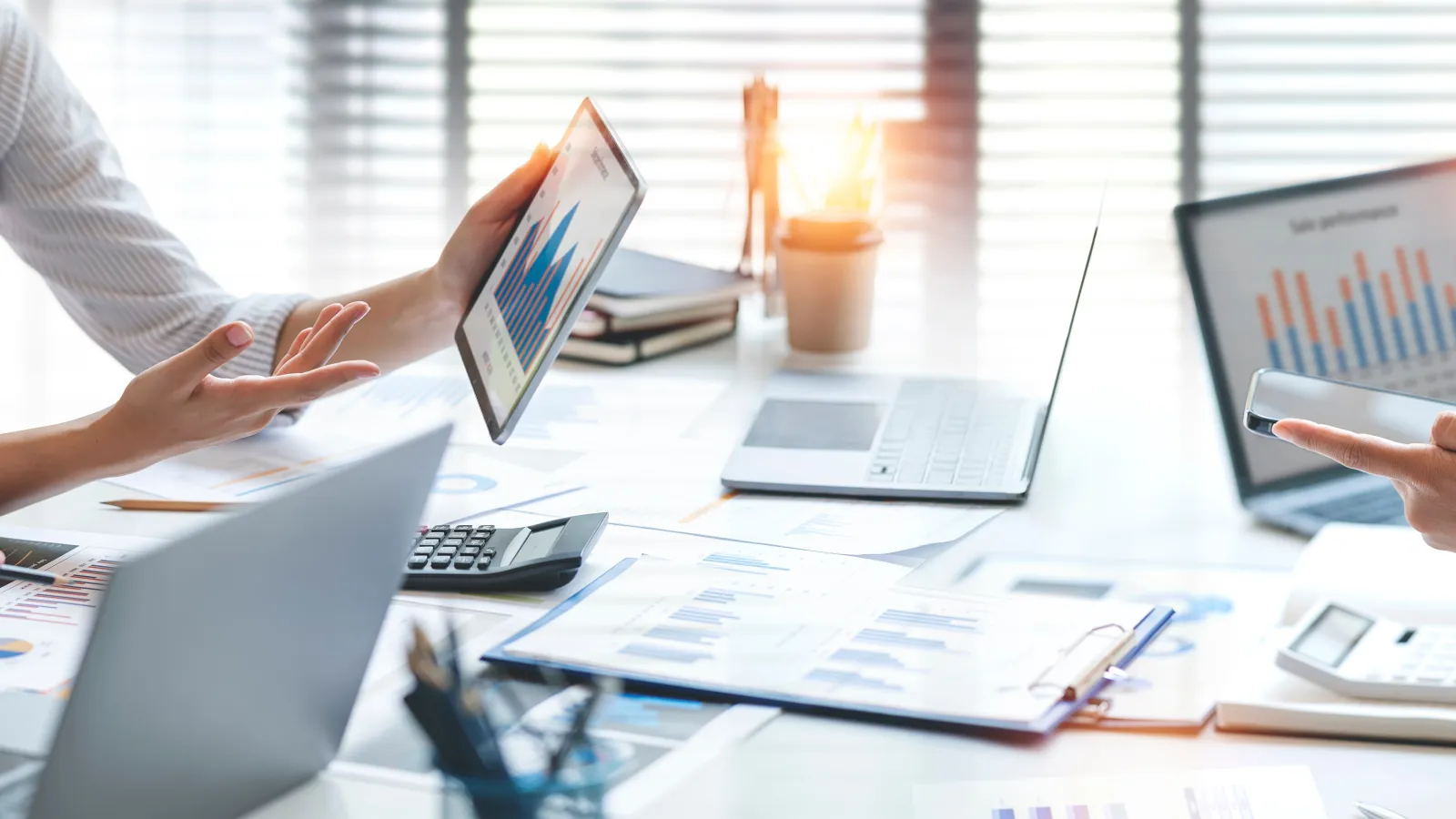 Business team analyzing charts and digital devices in a bright office meeting with laptops and tablets.