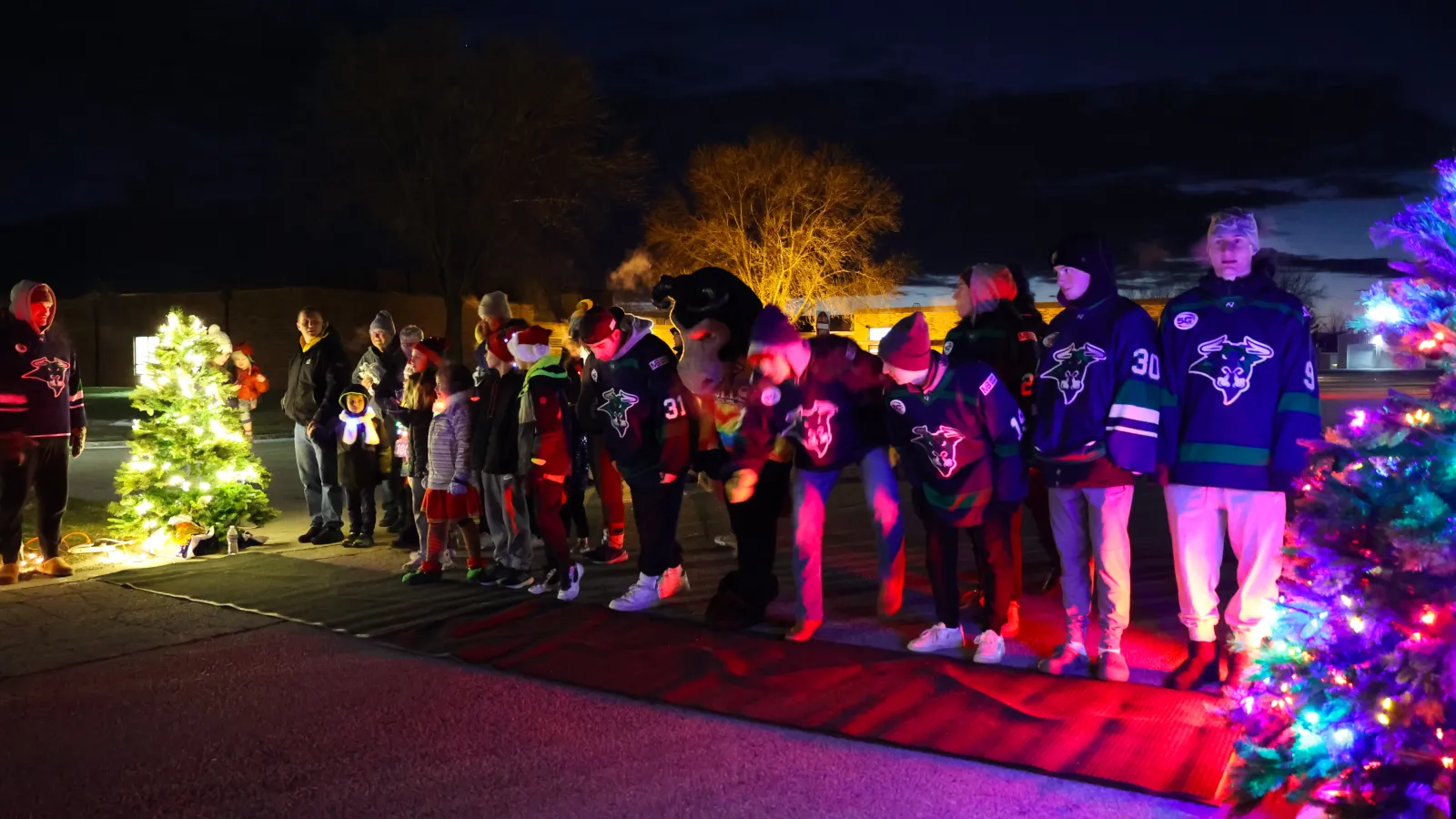 A festive scene with people in hockey jerseys celebrating under colorful lights and Christmas trees at night.