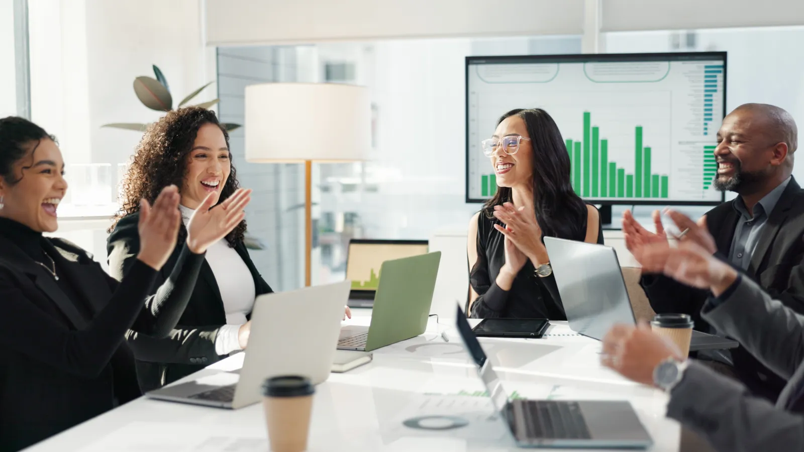 Diverse business team applauding during a meeting with laptops and green bar charts on screen