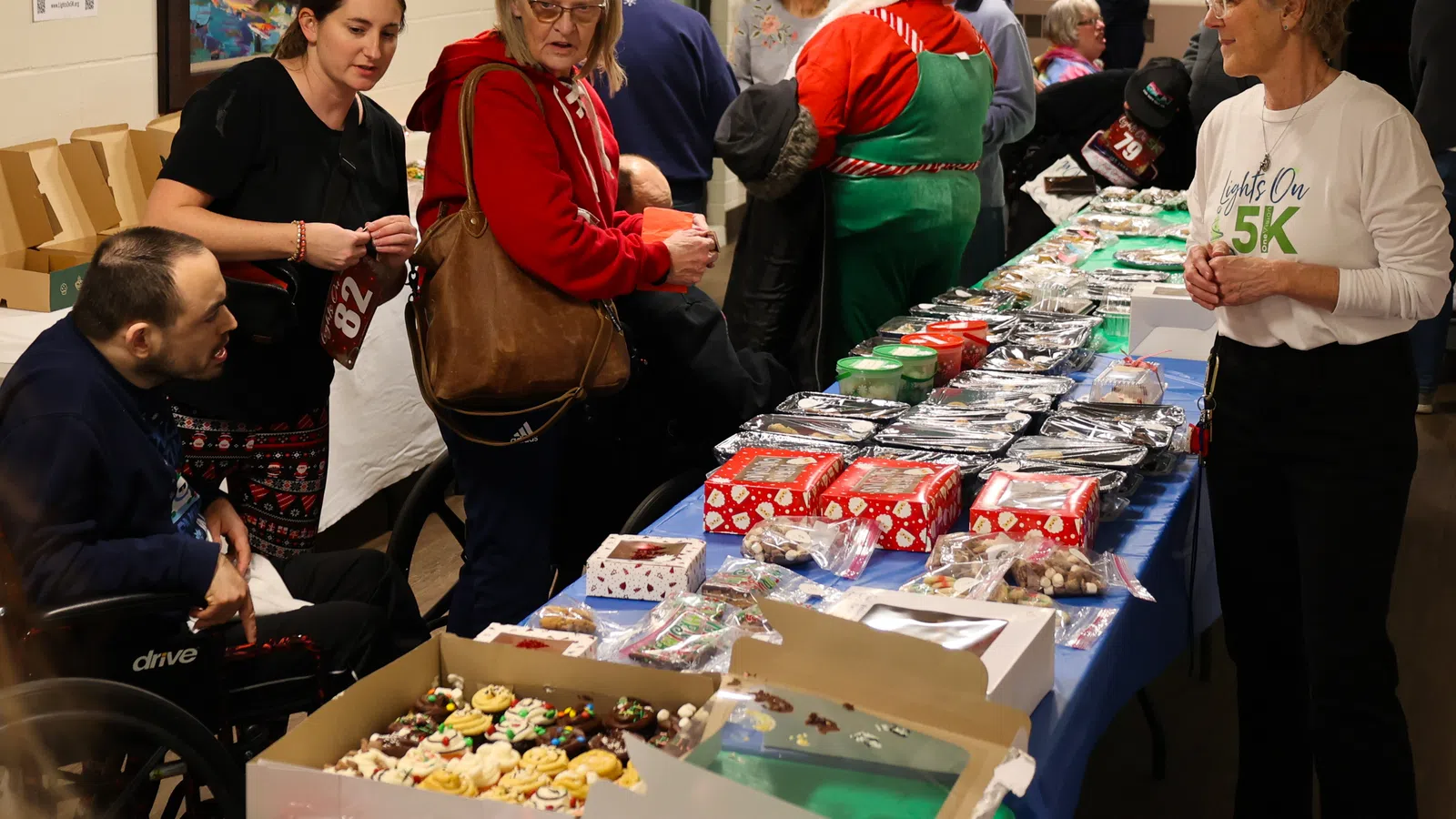 Community holiday market with people browsing festive goods and treats on tables.