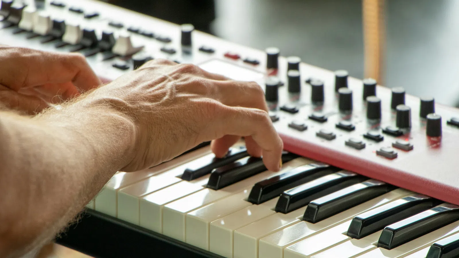 Close-up of hands playing a modern synthesizer keyboard with control knobs and buttons.