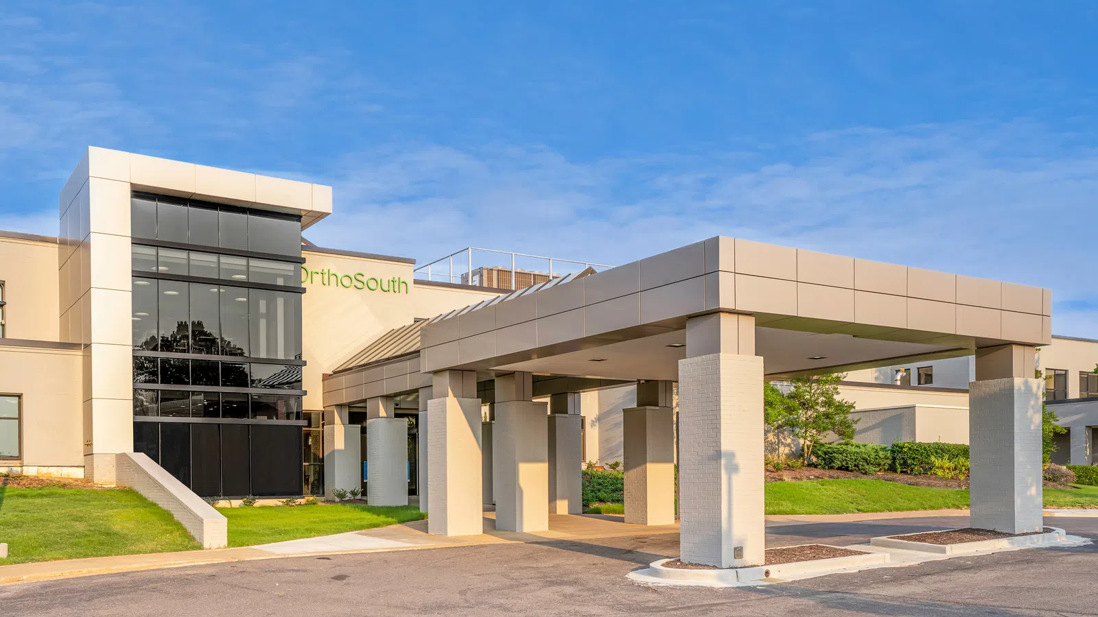 Modern medical building with large glass windows and covered entrance under clear blue sky.