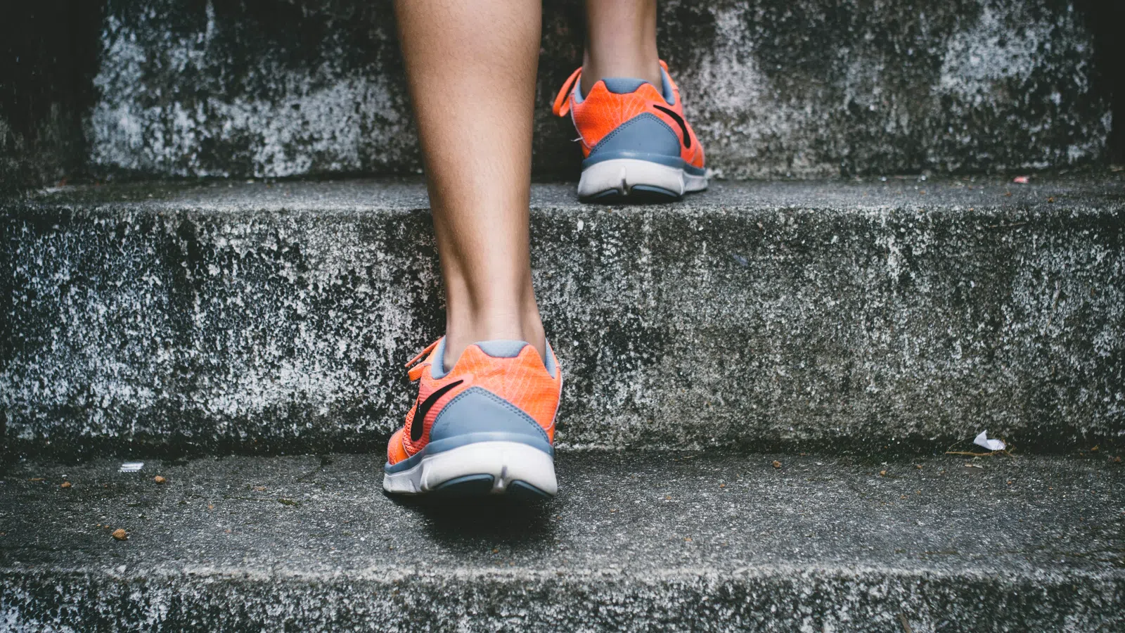 Person wearing orange and gray sneakers walking up concrete stairs with textured surfaces outdoors.