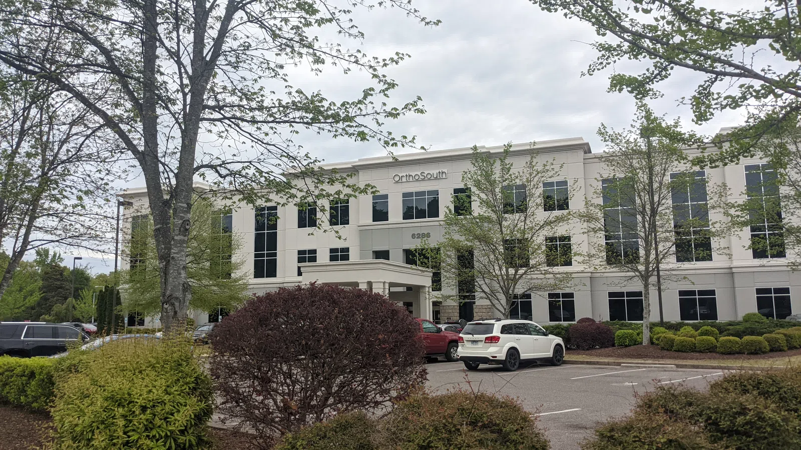 Modern three-story OrthoSouth medical office building with trees and parked cars on an overcast day