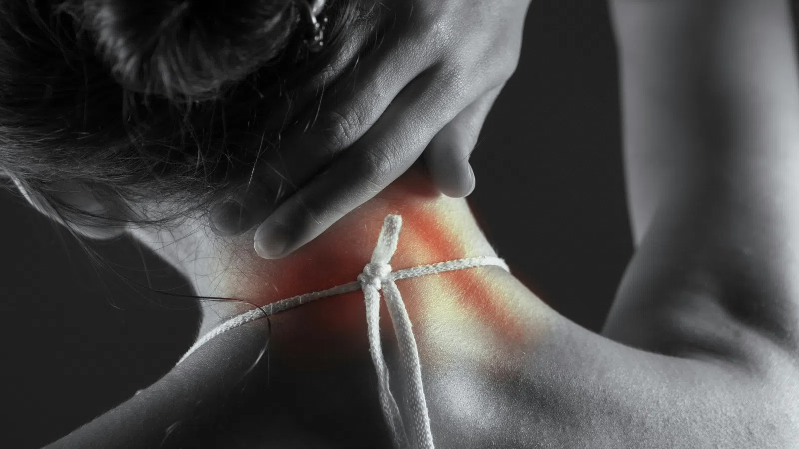 Person holding neck with highlighted red area indicating neck pain or discomfort in black and white photo.