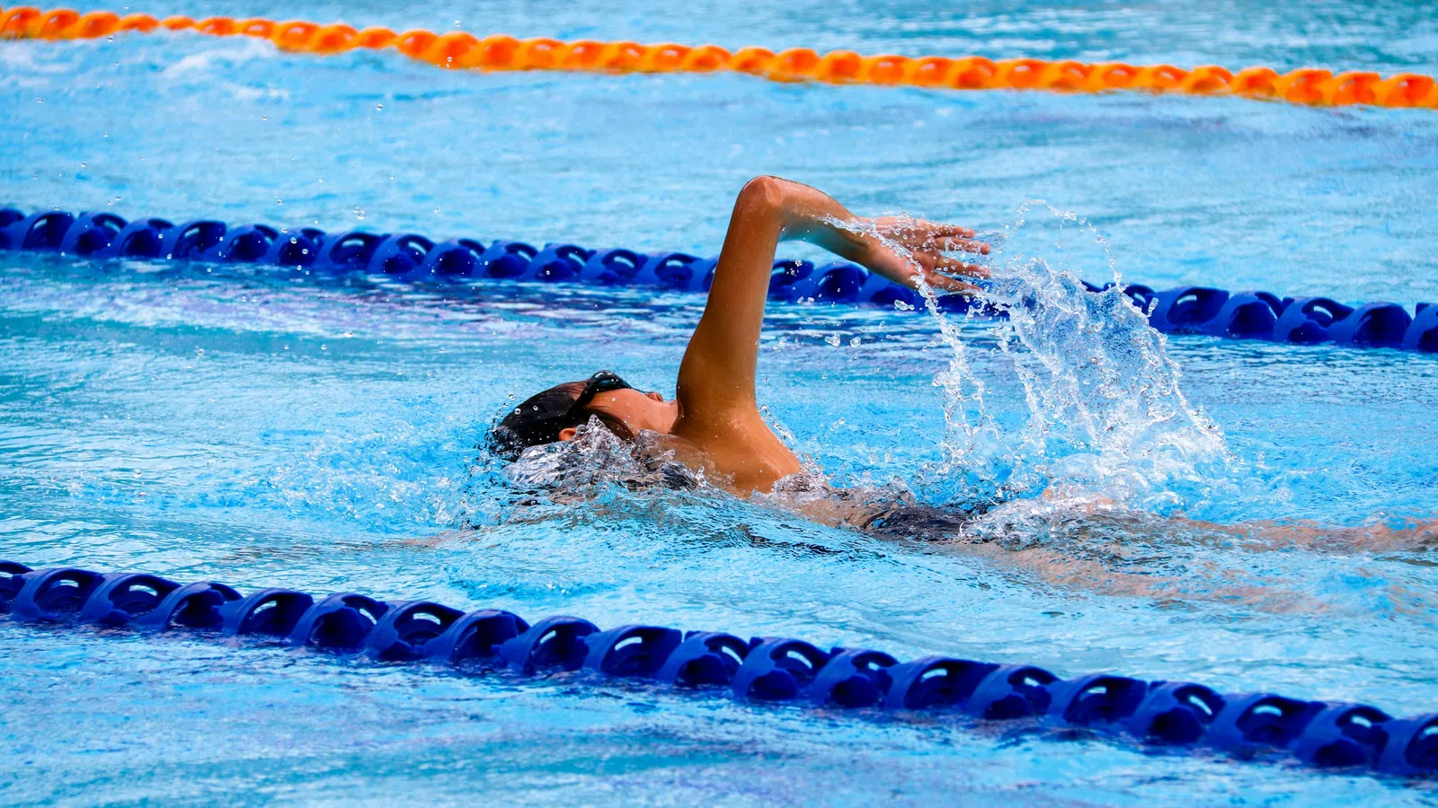 Swimmer performing backstroke in a pool lane with blue and orange lane dividers during a race.
