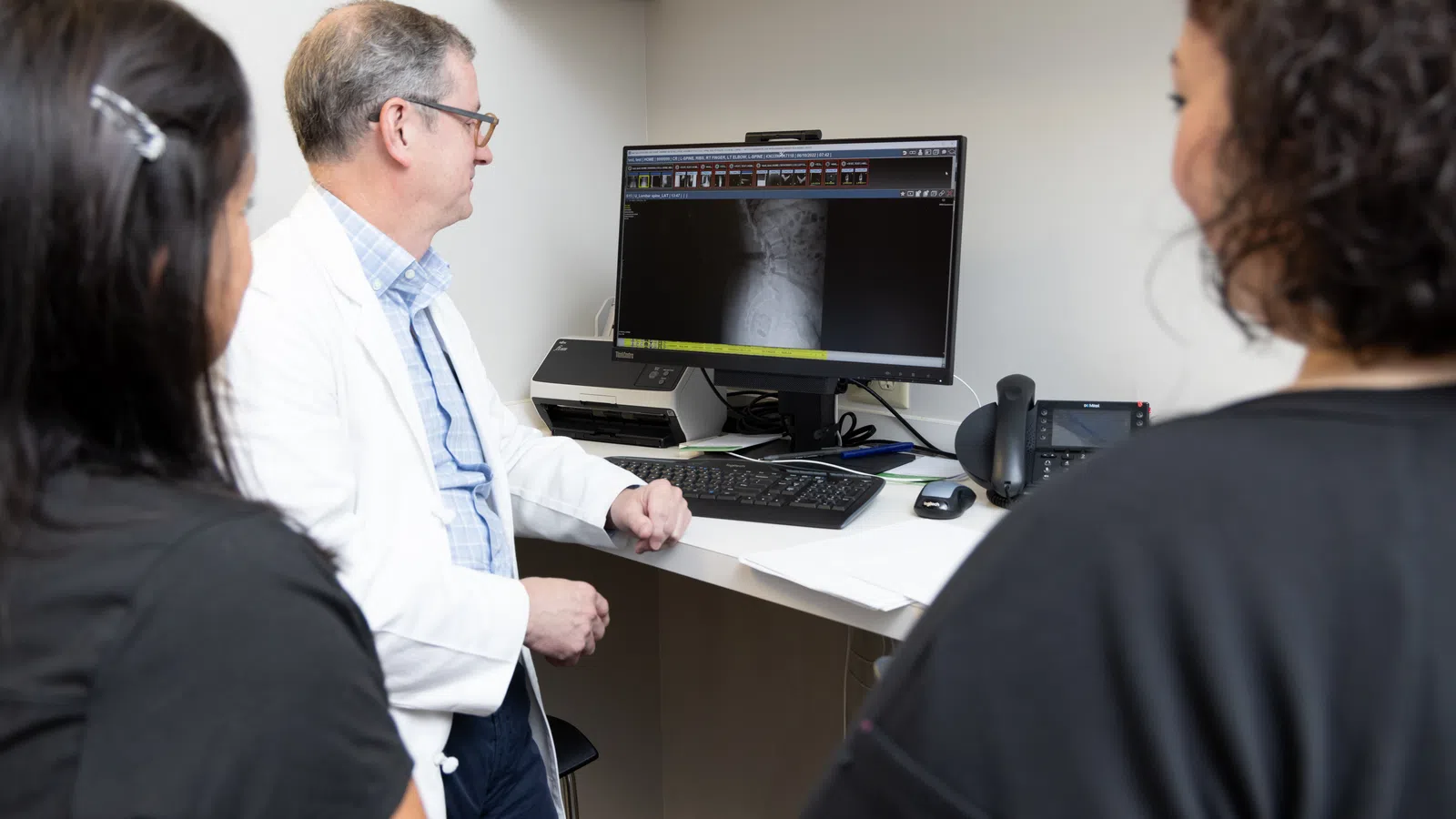 Doctor discussing medical imaging results with two patients in a clinic setting.